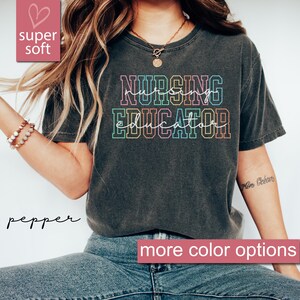 Puede incluir: Una camiseta gris oscuro con el texto "Nursing Educator" en colores arco&iacute;ris. El texto est&aacute; contorneado en blanco. La camiseta est&aacute; hecha de un material suave y c&oacute;modo.