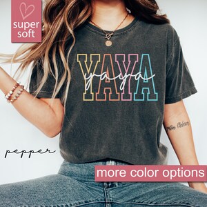 May include: A dark gray t-shirt with the word "YAYA" printed in rainbow colors. The text is outlined in black. The shirt is super soft and has a relaxed fit.