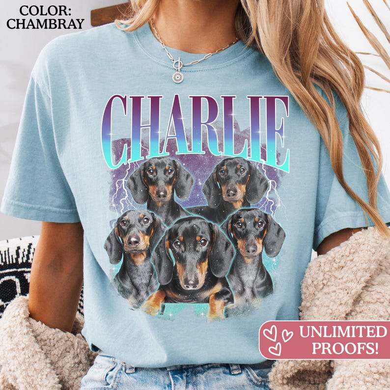 K&ouml;nnte beinhalten: Ein chambray-blaues T-Shirt mit einem Grafikdruck von f&uuml;nf schwarz-lohfarbenen Dackeln. &Uuml;ber den Hunden ist der Name CHARLIE in einer gro&szlig;en, fetten, violett-blauen Verlaufs-Schrift gedruckt. Das Design enth&auml;lt Blitze und Sterne.