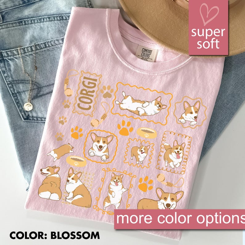 May include: A light pink t-shirt with a repeating pattern of Corgi dog illustrations in various poses, paw prints, and food bowls. The word "CORGI" is printed in a rectangular frame. The shirt is labeled "super soft" and "more color options".