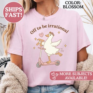 Könnte beinhalten: Hellrosa T-Shirt mit dem Text "Off to be irrational" und einer Cartoon-Gans auf einem rosa Roller. Die Gans trägt einen Blumenkranz und hält einen Hammer. Der Text "More Subjects Available!" ist ebenfalls vorhanden.