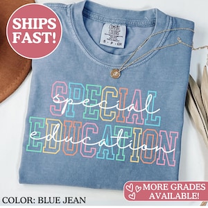 May include: Blue jean colored t-shirt with the words "Special Education" in colorful block letters. A gold necklace with a pendant rests on the shirt. The shirt has a vintage look and feel.