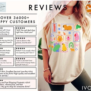 May include: Ivory-colored t-shirt featuring a colorful graphic of capybaras in postage stamp designs. The shirt includes the word "capybara" and is surrounded by text that reads "Reviews" and "Over 36000+ Happy Customers."