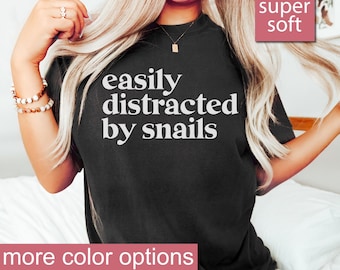 May include: A black t-shirt with the text "easily distracted by snails" in white. The shirt is super soft and has more color options.