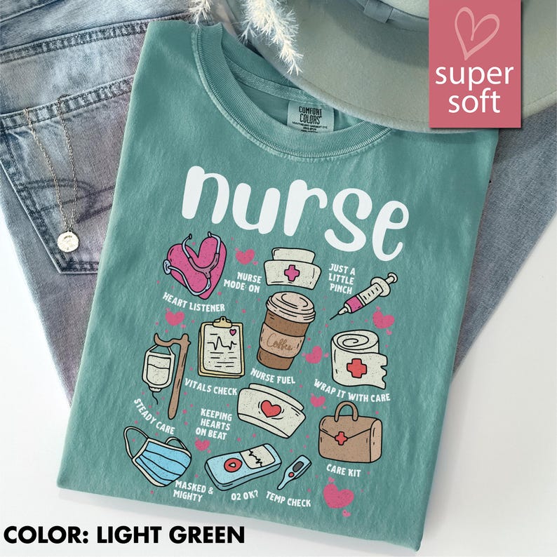May include: Light green t-shirt with the word "nurse" and various medical-themed illustrations. The shirt features a stethoscope, coffee cup, syringe, and other medical symbols. The text "super soft" is in a pink heart-shaped box.