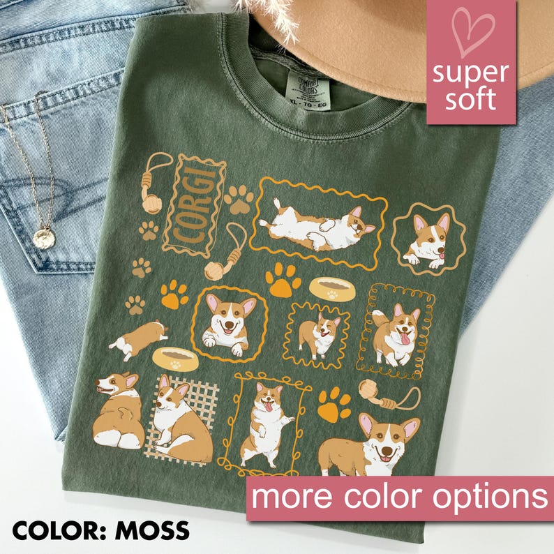 May include: Moss green t-shirt featuring a repeating pattern of Corgi dogs in various poses, paw prints, and dog toys. The word "CORGI" is printed in a rectangular frame. The shirt has a crew neck and short sleeves. The text "super soft" is in a pink box.