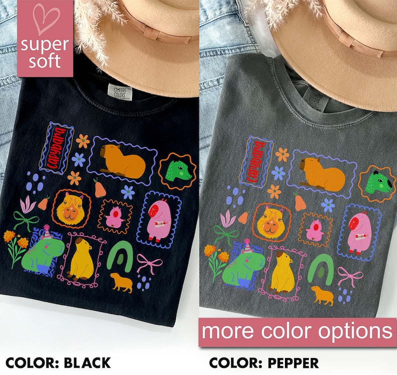 May include: Black and pepper-colored t-shirts with colorful capybara illustrations. The shirts feature various capybara designs within decorative frames, along with floral and geometric elements. The text "super soft" and "more color options" are also visible.