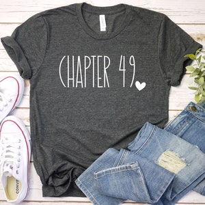 May include: A dark gray t-shirt with the text "CHAPTER 49" and a small white heart printed on the front.