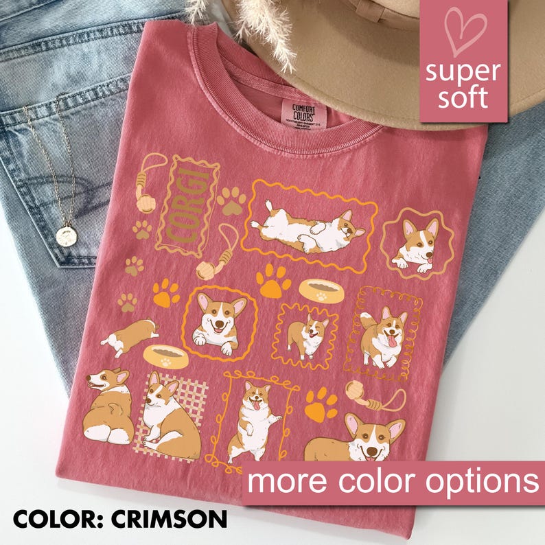 May include: Crimson-colored t-shirt featuring multiple framed illustrations of Corgi dogs in various poses, along with paw prints and dog bone graphics. The shirt also has the word "CORGI" in a rectangular frame. The text "more color options" is visible.