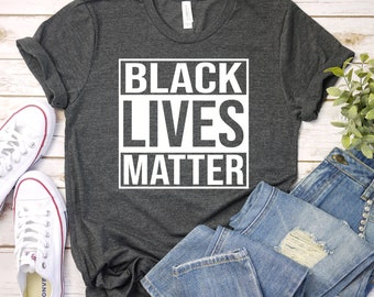 Puede incluir: Una camiseta gris oscura con las palabras "Black Lives Matter" impresas en blanco en un cuadro.