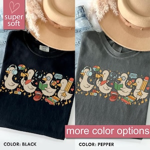 May include: Black and pepper-colored t-shirts with a graphic of cartoon ducks wearing headphones, holding books, and pencils. The shirts have the text "SPEECH" and "ABC". The image also includes the text "super soft" and "more color options".