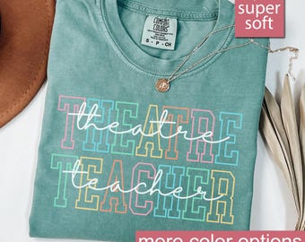 May include: Light green t-shirt with the text "theatre teacher" in rainbow colors. The shirt is made of a soft, comfortable fabric.