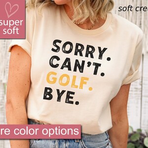 May include: A cream colored t-shirt with the text "SORRY. CAN'T. GOLF. BYE." in black and yellow. The text has a distressed look.
