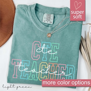 Könnte beinhalten: Hellgrünes T-Shirt mit dem Text "CTE Teacher" in Regenbogenfarben. Das Shirt ist aus weichem, bequemem Stoff.  "Super weich" und "mehr Farbmöglichkeiten" stehen in Rosa oben und unten im Bild.