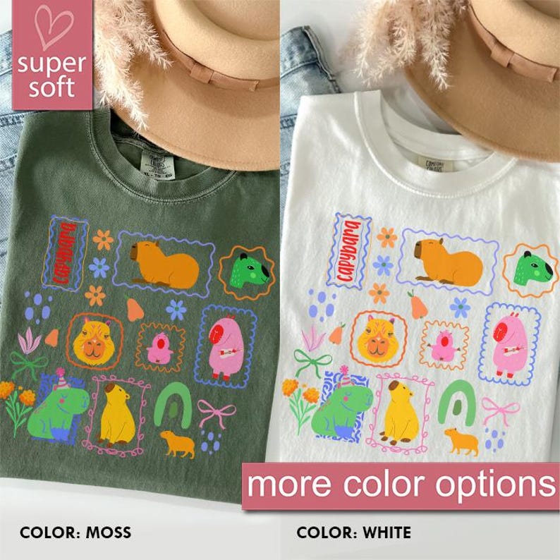 May include: Two t-shirts, one moss green and one white, featuring colorful capybara illustrations. The designs include various capybara characters within decorative frames, flowers, and the word "capybara". The shirts are labeled "super soft" and "more color options".