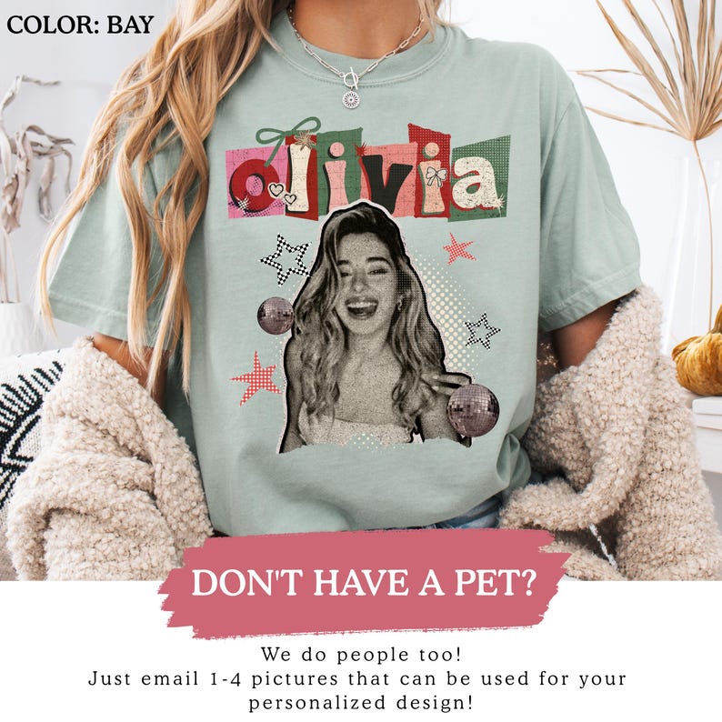 May include: A light green t-shirt with the name "Olivia" in a colorful, collage-style design. The shirt features a black and white image of a smiling person, disco balls, and star graphics. The text "DON'T HAVE A PET?" is also visible.