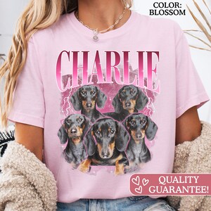 K&ouml;nnte beinhalten: Ein hellrosa T-Shirt mit dem Namen CHARLIE in gro&szlig;en rosa Buchstaben oben. Unter dem Text sind vier schwarz-braune Dackel in einer Gruppe vor einem rosa Hintergrund mit Blitz-Akzenten und Glitzereffekten abgebildet.