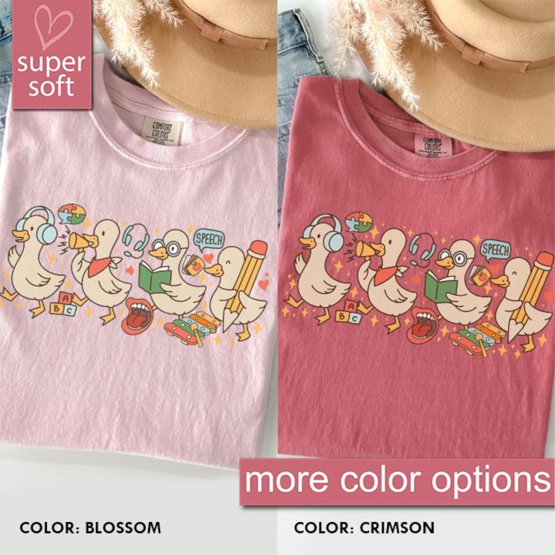 May include: Two t-shirts, one blossom pink and one crimson, featuring a cartoon duck design. The ducks wear headphones, read books, and hold pencils. The text "super soft" and "more color options" are also visible.