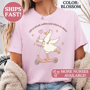 Könnte beinhalten: Hellrosa T-Shirt mit einer Cartoon-Krankenschwester-Gans auf einem Roller, die eine Spritze hält. Der Text lautet: "Off to drink coffee and chart at dawn." Der Text "MORE NURSES AVAILABLE!" ist ebenfalls vorhanden.