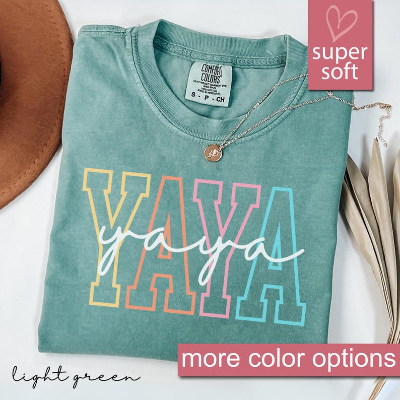 May include: A light green t-shirt with the word "YAYA" printed in rainbow colors. The shirt is made of a soft, comfortable fabric and has a relaxed fit.