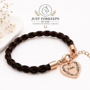 May include: A braided dark brown hair bracelet featuring rose gold-toned metal end caps, a lobster clasp, and an adjustable chain. A heart-shaped rose gold-toned charm is attached, engraved with the name Rikki surrounded by a floral wreath design.