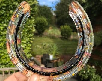 May include: A clear resin horseshoe with dried flowers and gold glitter embedded inside. The horseshoe is a decorative object.