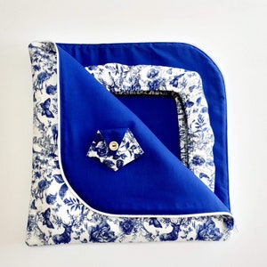 May include: A blue and white baby changing mat with a blue fabric cover and a white fabric lining. The cover has a pocket on the front. The lining features a blue and white floral pattern with deer and butterflies.