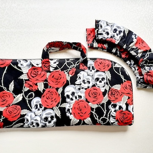 May include: Black zippered bag with a skull and rose design. The bag has a handle and is made of fabric.