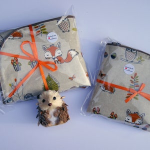 May include: Two fabric gift bags with a woodland animal print. The bags are tied with orange ribbon and feature owls, foxes, and hedgehogs. The bags are packaged in clear plastic.