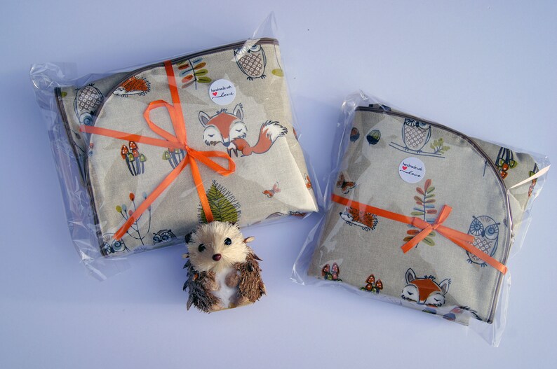 May include: Two fabric gift bags with a woodland animal print. The bags are tied with orange ribbon and feature owls, foxes, and hedgehogs. The bags are packaged in clear plastic.