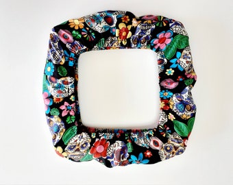 May include: A black fabric chair cover with a colorful Day of the Dead pattern featuring sugar skulls, flowers, and leaves.