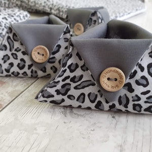 Peut inclure: Trois paniers de rangement triangulaires en tissu gris avec un motif léopard. Chaque panier a un bouton en bois avec le texte "Handmade with love" dessus.