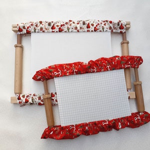 May include: Two wooden embroidery hoops with red and white fabric. The smaller hoop is inside the larger hoop.