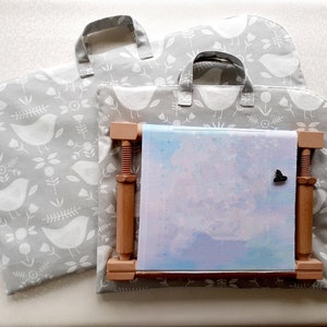 May include: Two grey fabric storage bags with white bird and floral patterns and a wooden embroidery hoop with a light blue and pink canvas inside.