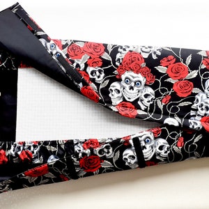 May include: A black canvas embroidery hoop with a skull and red rose print. The hoop is open and the fabric is visible.