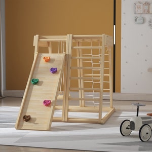 May include: Wooden indoor playset with a slide, climbing wall, and rope ladder. The slide has colorful climbing holds. The playset is made of natural wood and is suitable for indoor use.