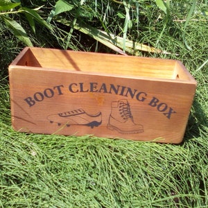 May include: A wooden box with the words "BOOT CLEANING BOX" printed on the front. The box has a brown stain and is decorated with a black silhouette of a boot and a shoe.