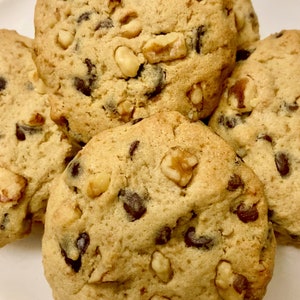 May include: Close-up of four chocolate chip cookies with walnuts. The cookies are golden brown and have a slightly crispy texture.