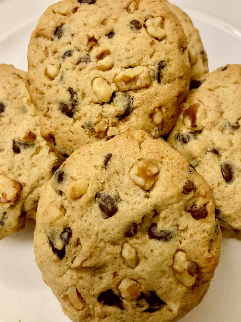 May include: Close-up of four chocolate chip cookies with walnuts. The cookies are golden brown and have a slightly crispy texture.