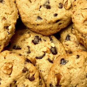 May include: Close-up of a pile of chocolate chip cookies with walnuts. The cookies are golden brown and have a slightly crispy texture.