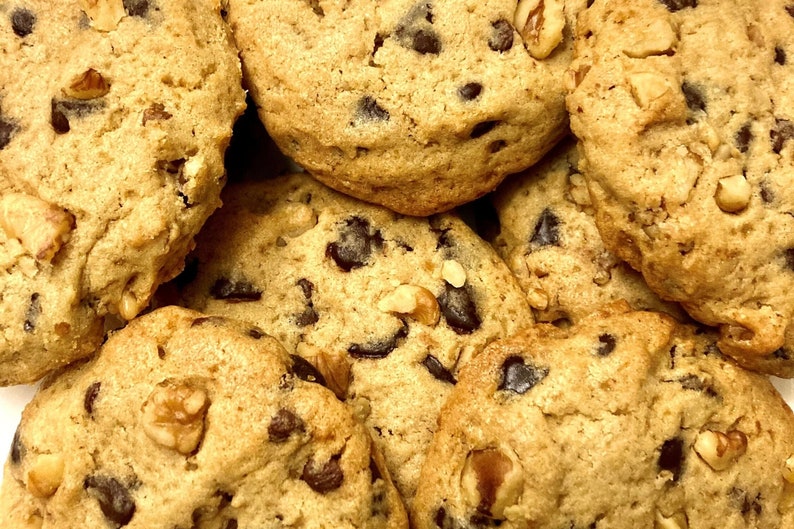 May include: Close-up of a pile of chocolate chip cookies with walnuts. The cookies are golden brown and have a slightly crispy texture.