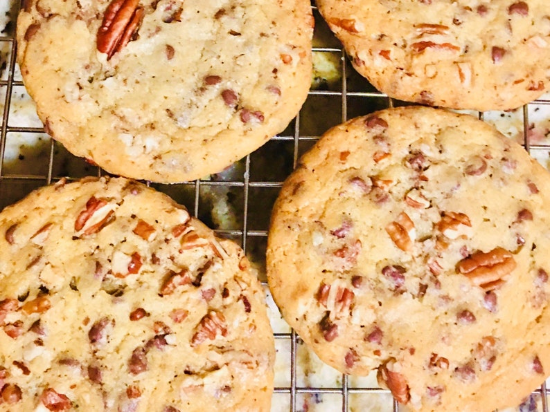 May include: Four golden brown chocolate chip cookies with pecans on a wire rack. The cookies are slightly domed and have a crispy texture.
