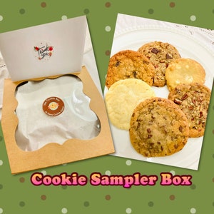 May include: A brown cardboard box with a clear window showing a variety of cookies. The box has a sticker that says "The Cookie Box" and "No Guilt Cookie Cravings". The cookies are arranged on a white plate. The cookies include chocolate chip, oatmeal raisin, peanut butter, and sugar cookies.