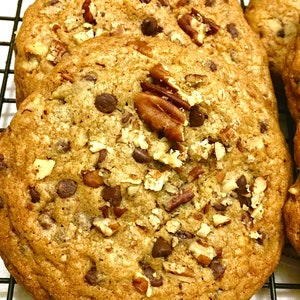 May include: Close-up of a stack of chocolate chip cookies with pecans on a black wire rack. The cookies are golden brown and have a crispy texture.