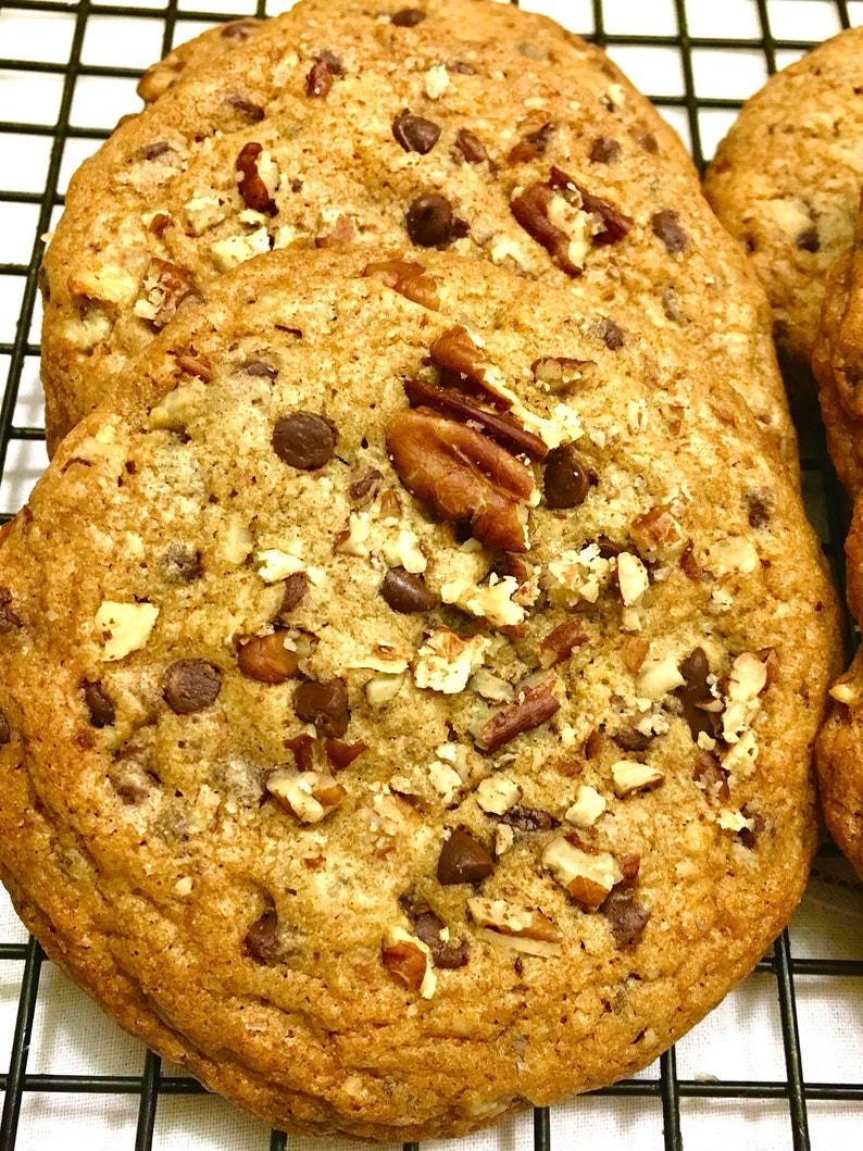May include: Close-up of a stack of chocolate chip cookies with pecans on a black wire rack. The cookies are golden brown and have a crispy texture.