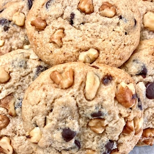 May include: Close-up of a pile of chocolate chip cookies with walnuts. The cookies are golden brown and have a slightly crispy texture.