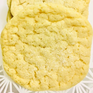 May include: A close-up of a light yellow sugar cookie with a slightly rough texture. The cookie is covered in a fine layer of sugar crystals.