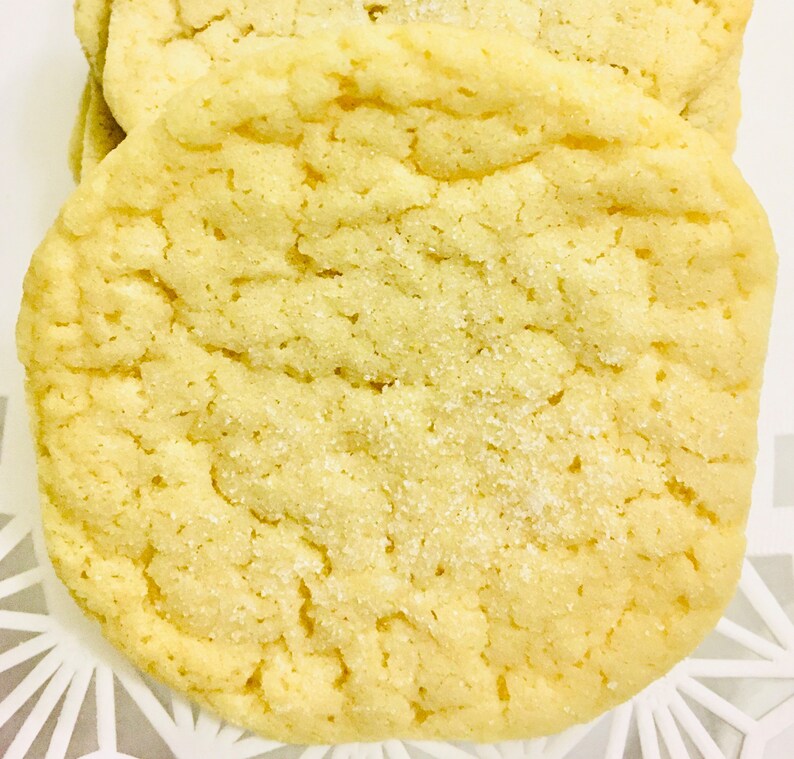 May include: A close-up of a light yellow sugar cookie with a slightly rough texture. The cookie is covered in a fine layer of sugar crystals.