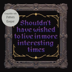 May include: Cross-stitch design with the text "Shouldn't have wished to live in more interesting times" in purple on a black background. The design is framed in a decorative, ornate, dark grey frame. A white circle in the upper left corner says "Compatible with Pattern Keeper."