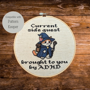 Può includere: Telaio da ricamo a punto croce con un gatto mago dei cartoni animati e la scritta "Current side quest brought to you by ADHD". Il gatto indossa un cappello e un mantello da mago blu. Un'etichetta circolare recita "Compatible with Pattern Keeper".